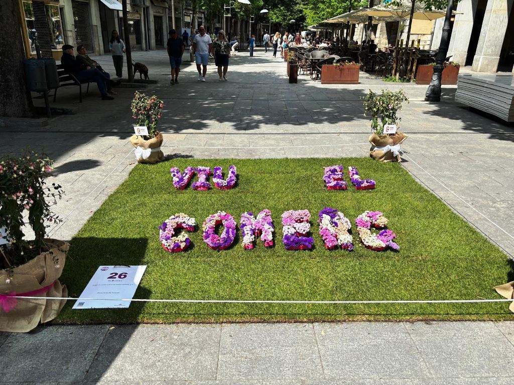 Un quadrat de gespa al terra i sobre un text amb flors que diu: viu el comerç